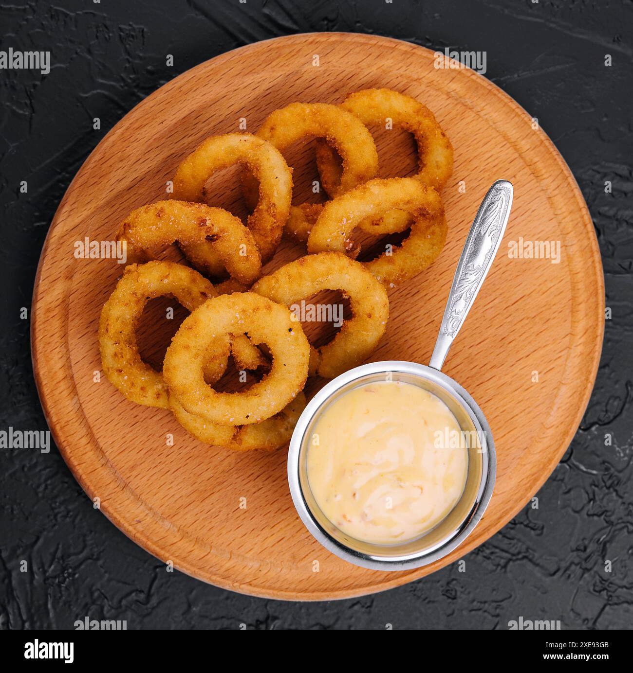 Anelli di cipolla fritti croccanti e salsa su piatto di legno Foto Stock