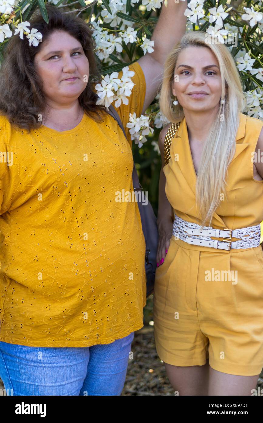 Questa immagine cattura due donne bionde vestite di giallo, che irradiano calore ed eleganza. Foto Stock