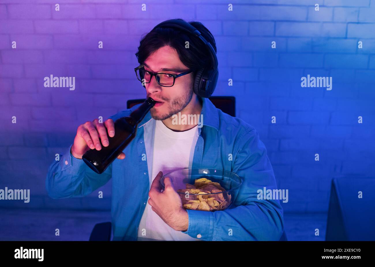 Il giovane beve birra e mangia patatine mentre gioca Foto Stock