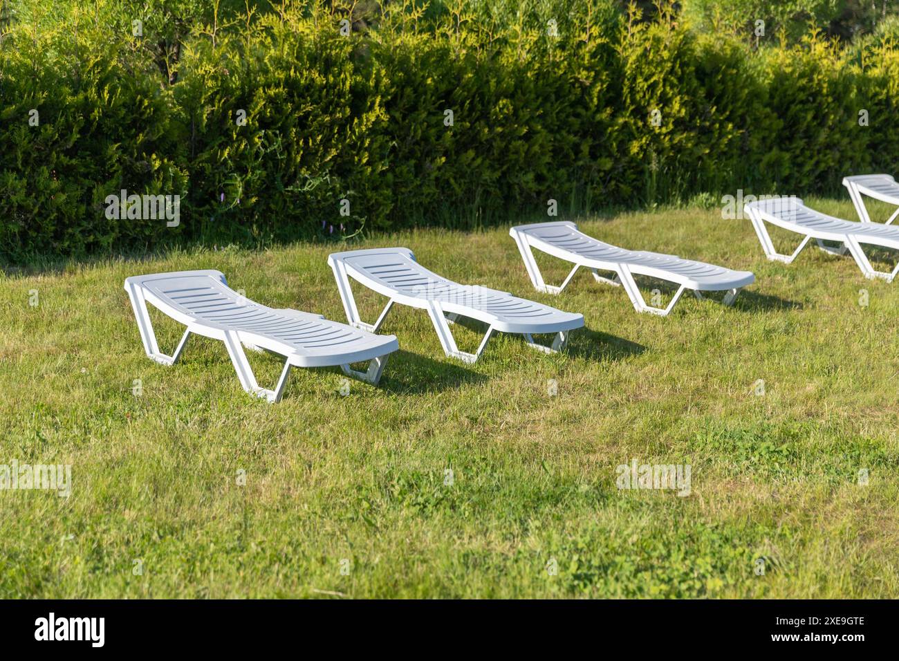 In una giornata di sole, i lettini bianchi in plastica si trovano in fila sull'erba verde Foto Stock