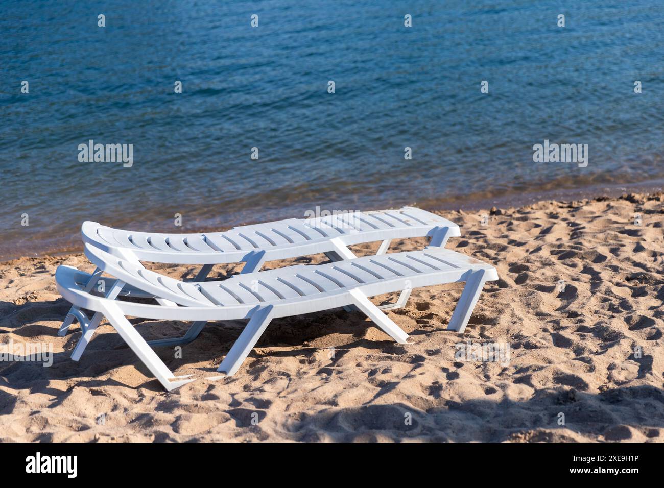 Due lettini bianchi in plastica si trovano su una spiaggia sabbiosa in una giornata di sole Foto Stock