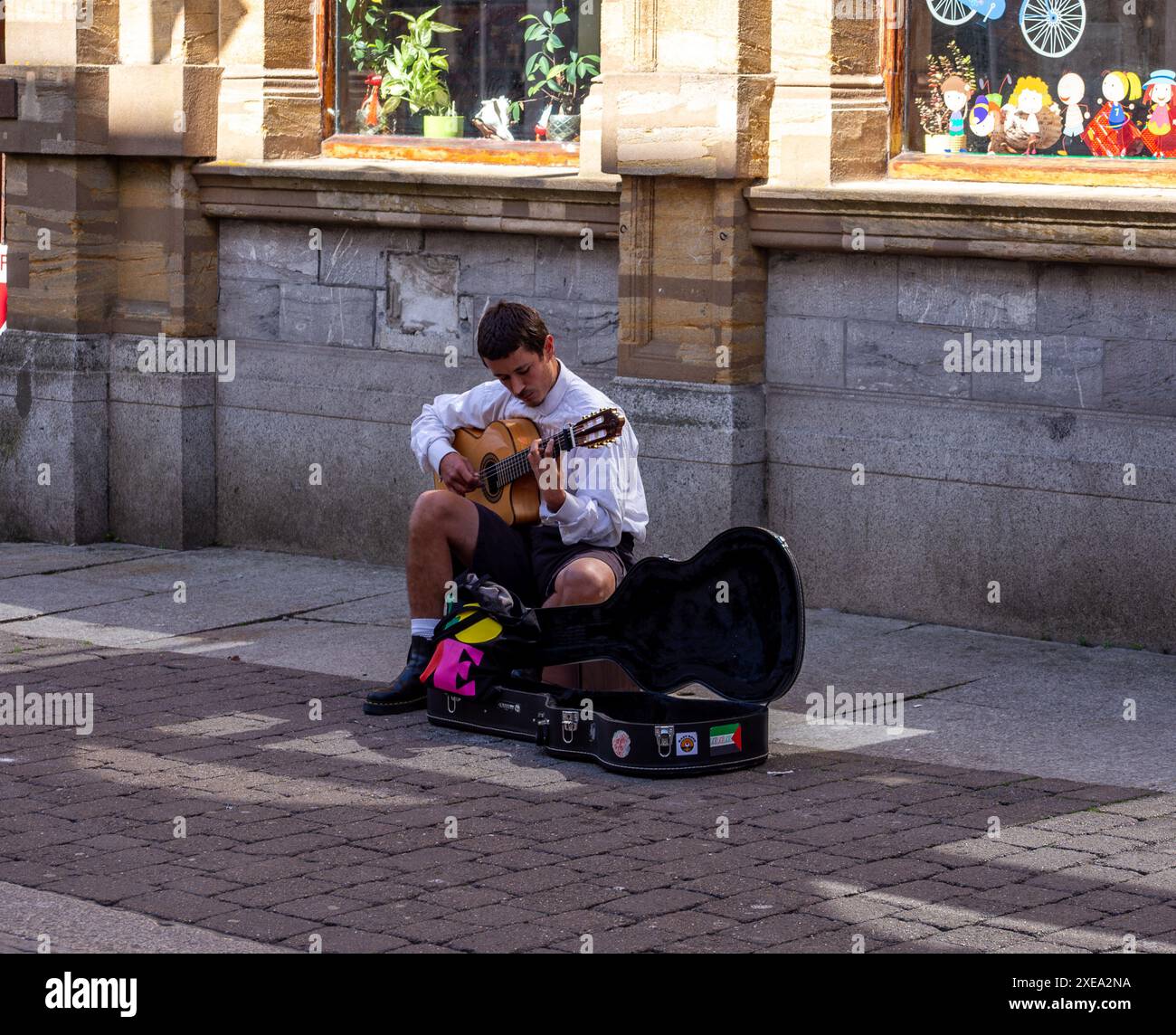 Musicista di strada che suona la chitarra in una giornata di sole in un ambiente urbano, con colorata confezione regalo e strada acciottolata Falmouth Cornwall Foto Stock