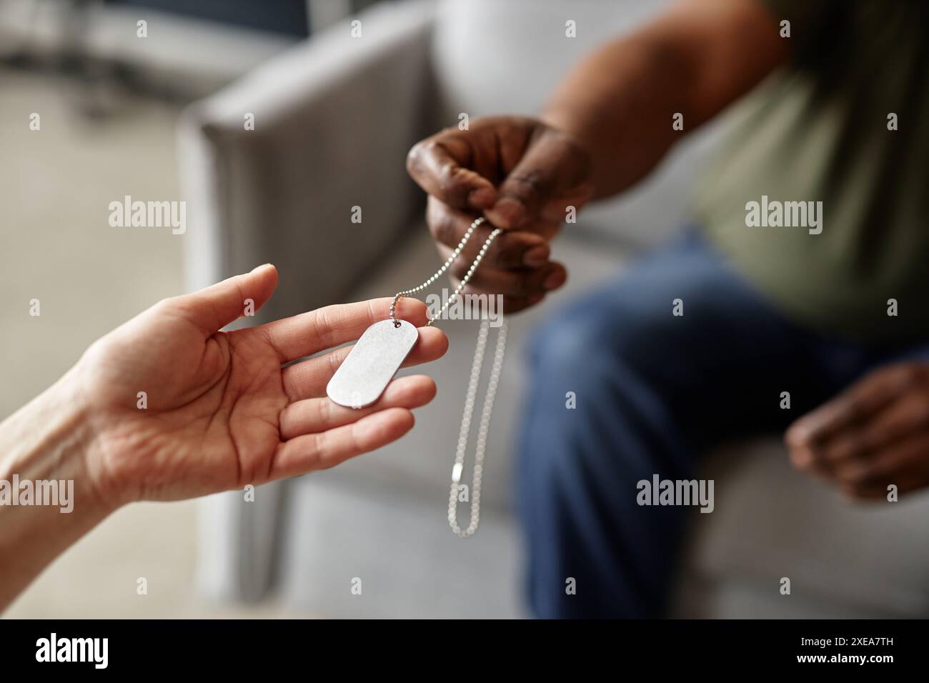 Primo piano di una mano femminile che regge delicatamente la collana di targhette per cani offerta dal veterano dell'esercito in uno spazio di copia sfocato sullo sfondo Foto Stock