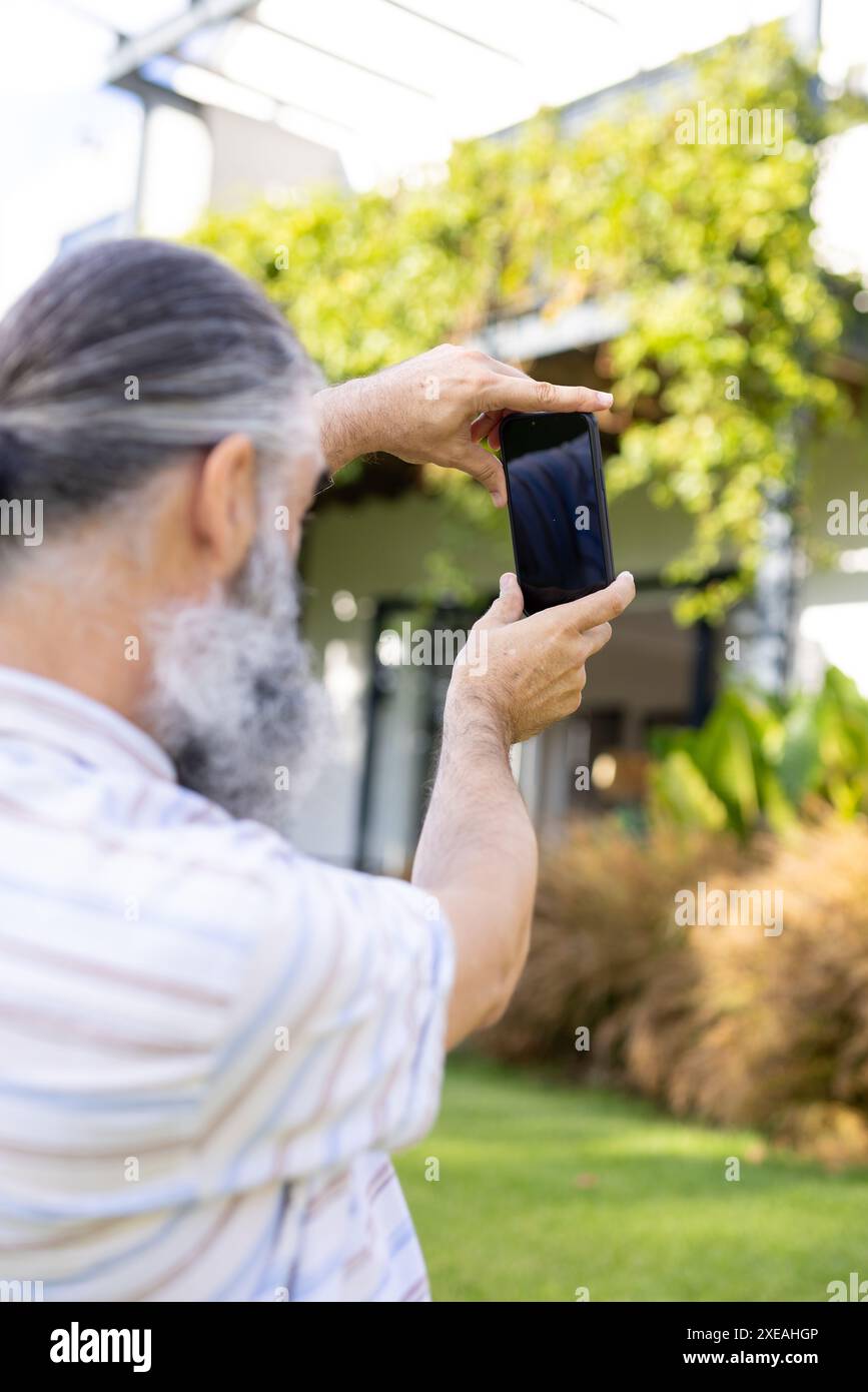 Scattare foto con lo smartphone, un anziano che cattura scene all'aperto in giardino, copiare spazio Foto Stock