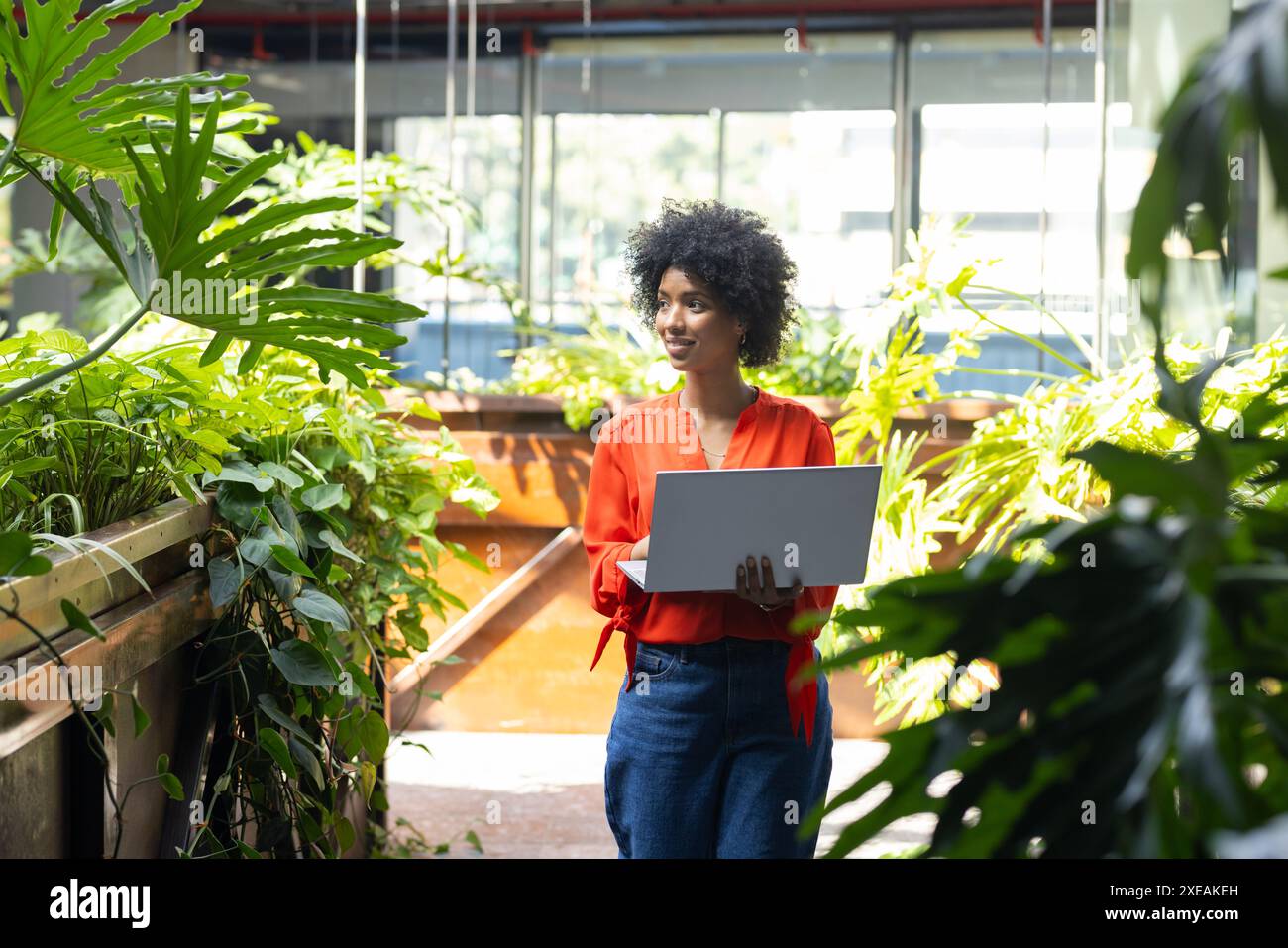In possesso di un computer portatile o di una donna che lavora in un lussureggiante giardino interno Foto Stock