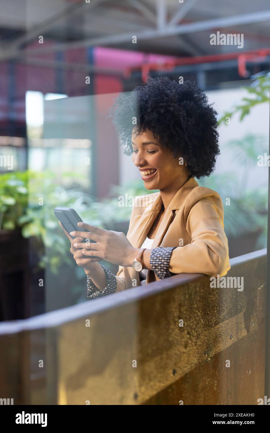 Donna d'affari afroamericana sorridente, che utilizza lo smartphone in un ufficio moderno Foto Stock