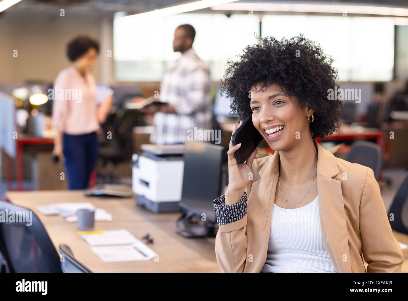Parla sullo smartphone, una donna d'affari afroamericana sorridente in un ufficio moderno Foto Stock