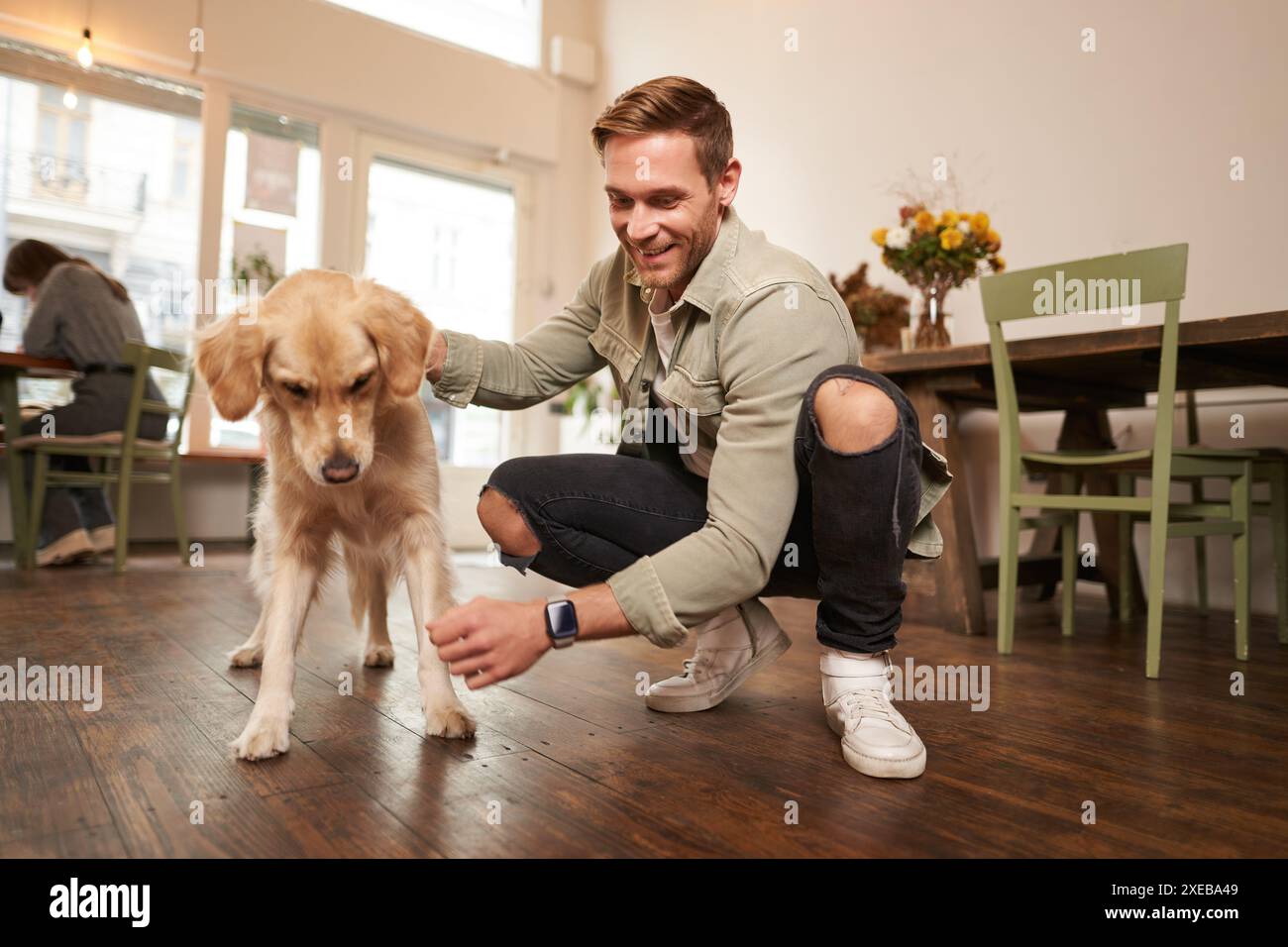 Ritratto di un uomo felice che trascorre del tempo con il suo cane in un bar in cui sono ammessi gli animali domestici, gioca e accarezza Golden retriever, divertiti, regalando Foto Stock