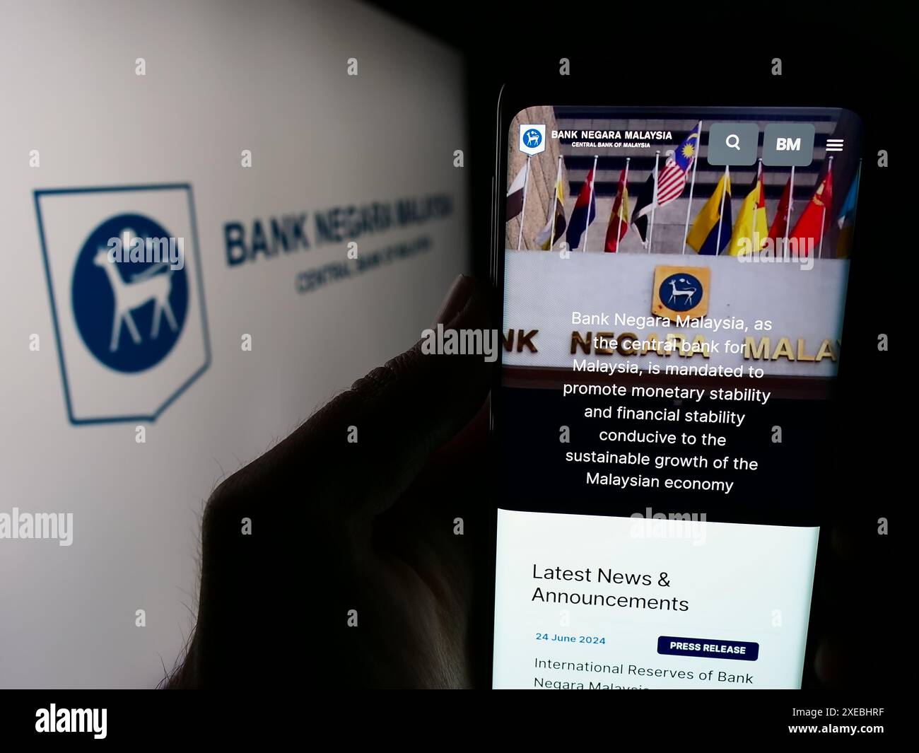 Persona che detiene un cellulare con pagina web della Malaysian Institution Bank Negara Malaysia (BNM) davanti al logo. Messa a fuoco al centro del display del telefono. Foto Stock