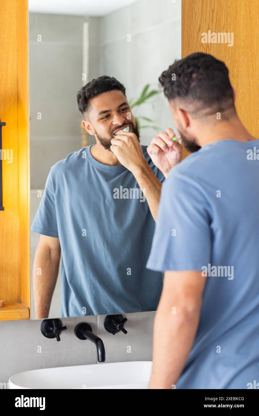 A casa, lavarsi i denti, l'uomo che guarda allo specchio e sorridere nel bagno moderno Foto Stock