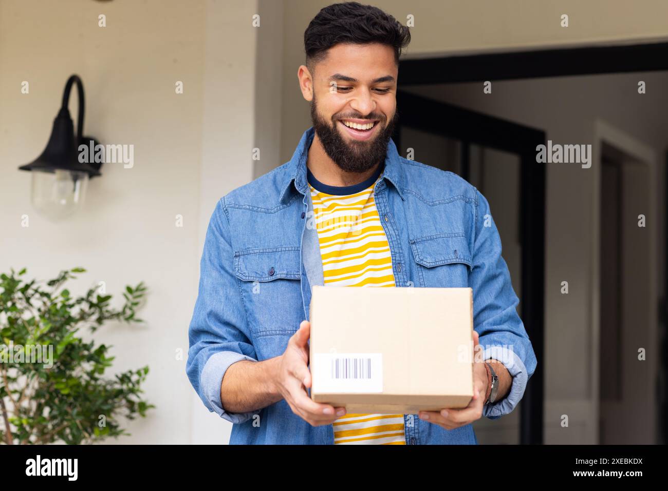 Fuori da casa sua, ricevendo pacco, uomo sorridente in piedi all'ingresso di casa Foto Stock