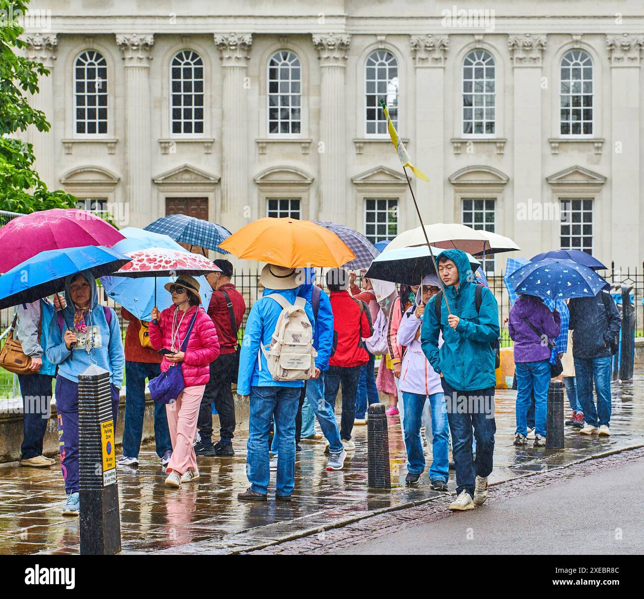 Un gruppo itinerante di turisti cinesi al di fuori della camera del Senato, dell'Università di Cambridge, in Inghilterra, in una giornata piovosa e umida. Foto Stock