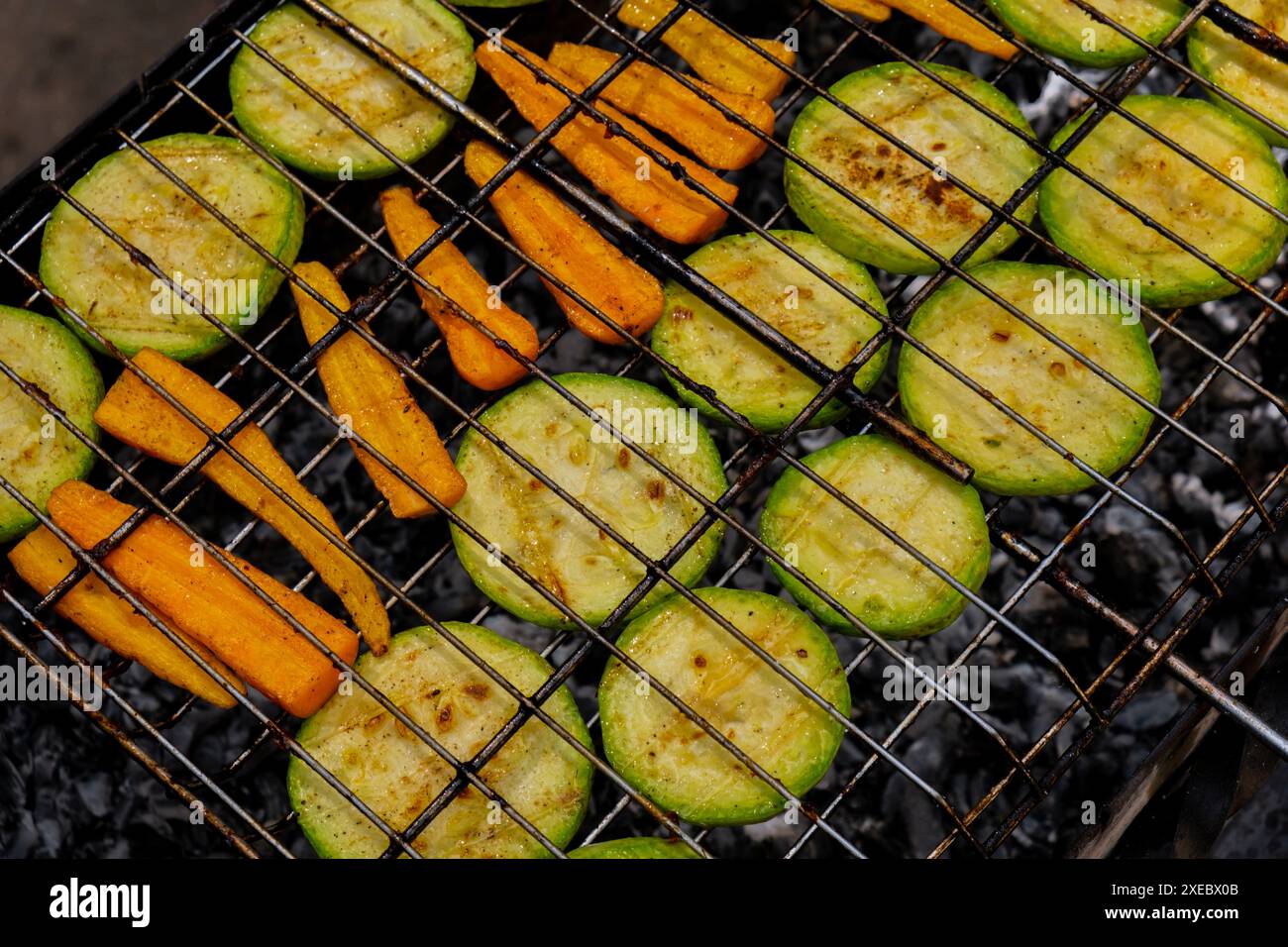 Zucchine tritate e carote arrostite sul fuoco condite con erbe aromatiche e spezie. Deliziose verdure fresche grigliate su barbe Foto Stock