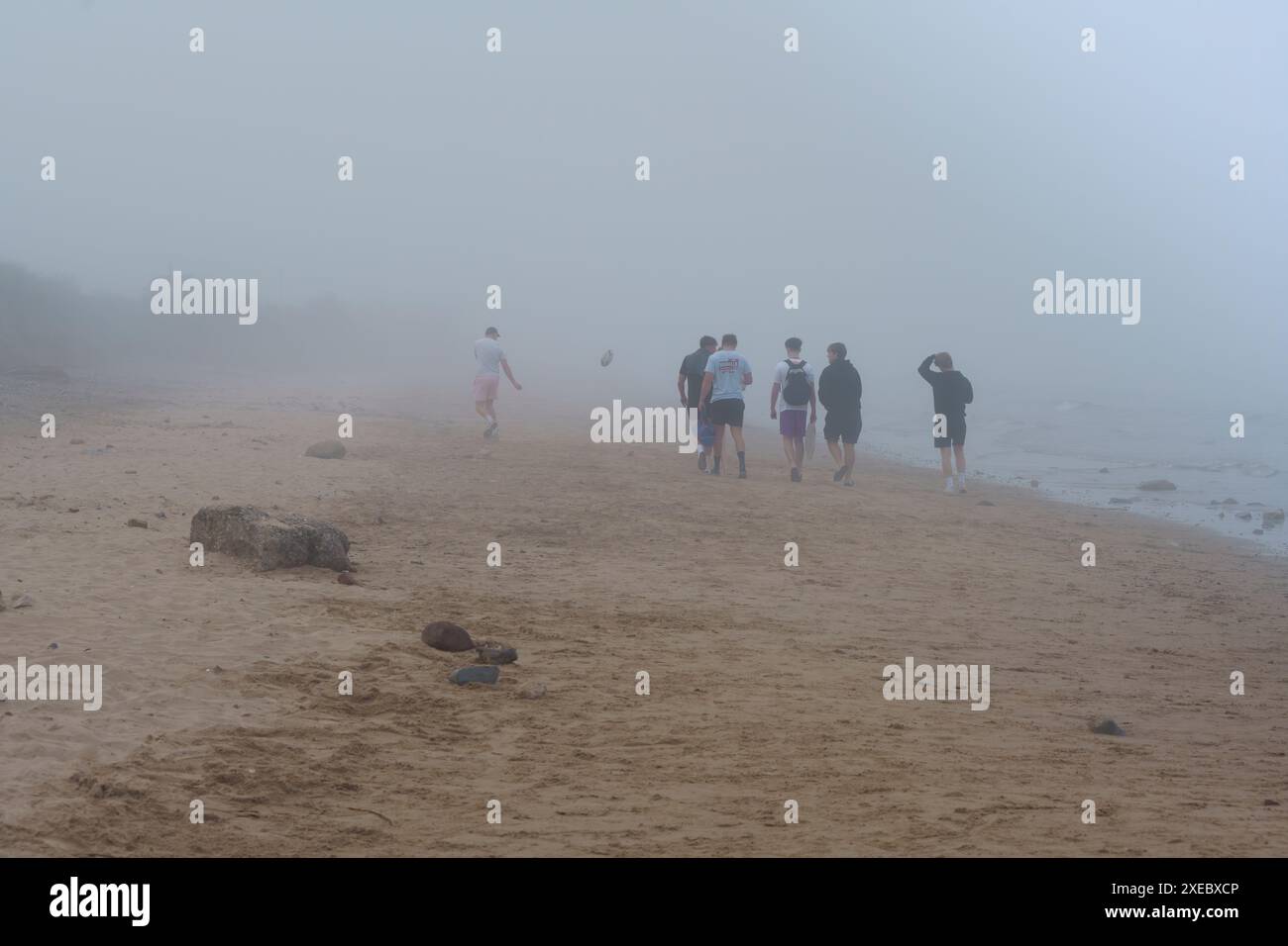 Un gruppo di giovani amici maschi bianchi si divertono a fare una passeggiata lungo la spiaggia di Fraisthorpe, nel tardo pomeriggio in una nebbia estiva. Costa dello Yorkshire orientale Foto Stock