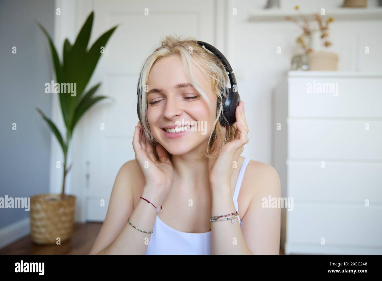 Concetto di persone e stile di vita, primo piano di una bella donna bionda con le cuffie wireless, ascolta musica e gode di buona qualità Foto Stock