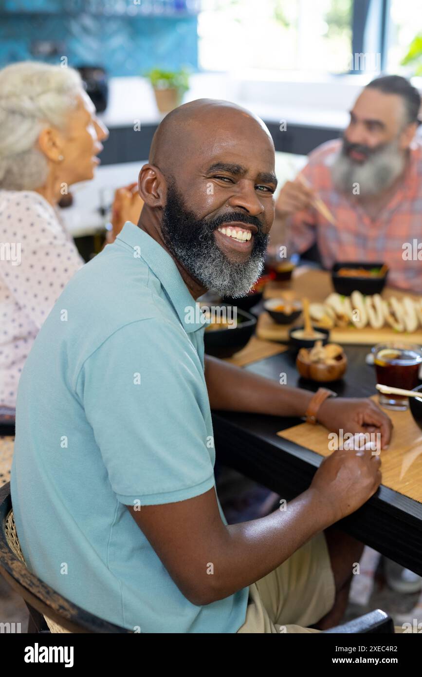 A casa, un uomo sorridente che gusta un pasto con amici anziani a tavola, divertendosi Foto Stock