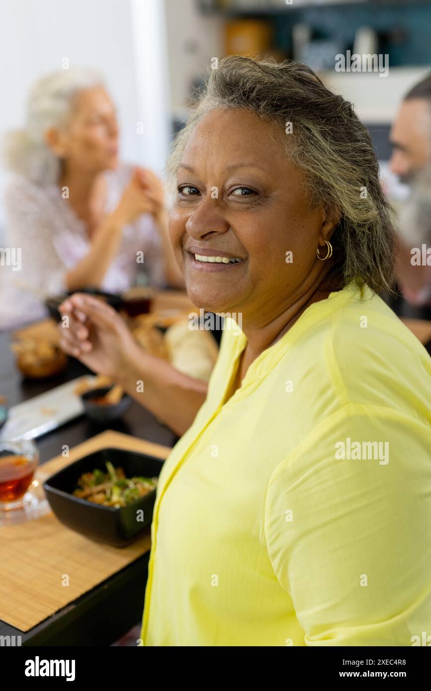 A casa, una donna sorridente che gusta un pasto con gli amici a tavola, condividendo i momenti Foto Stock