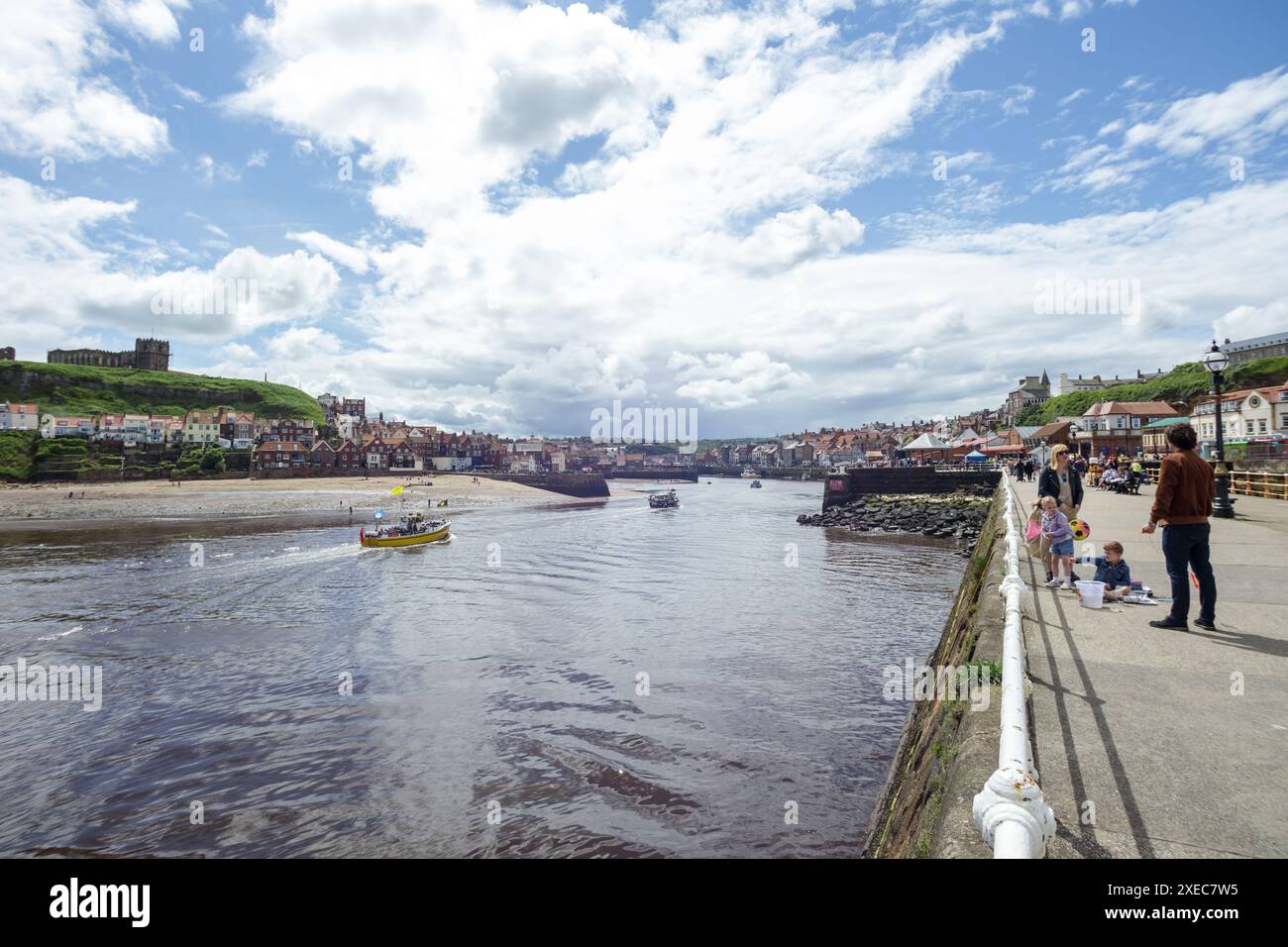 Una giovane famiglia pratica l'arte del granchio a Whitby Harbour mentre una barca da crociera di piacere naviga con Whitby Abbey sullo sfondo Foto Stock