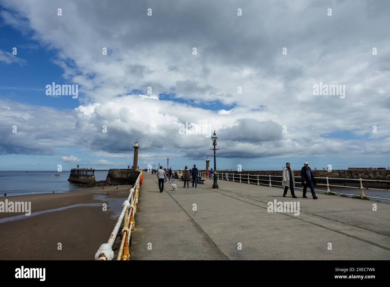 Gli escursionisti di un giorno passeggiano per le mura del porto e ammirano l'aria di mare in questo Bank Holiday di fine maggio a Whitby, casa della leggenda di Dracula. Foto Stock