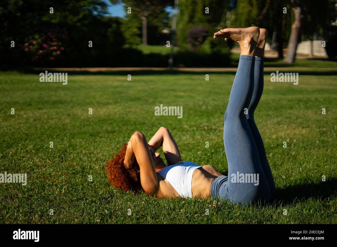 Donna che fa esercizi ipopressivi e pilates sdraiati sull'erba in un parco Foto Stock
