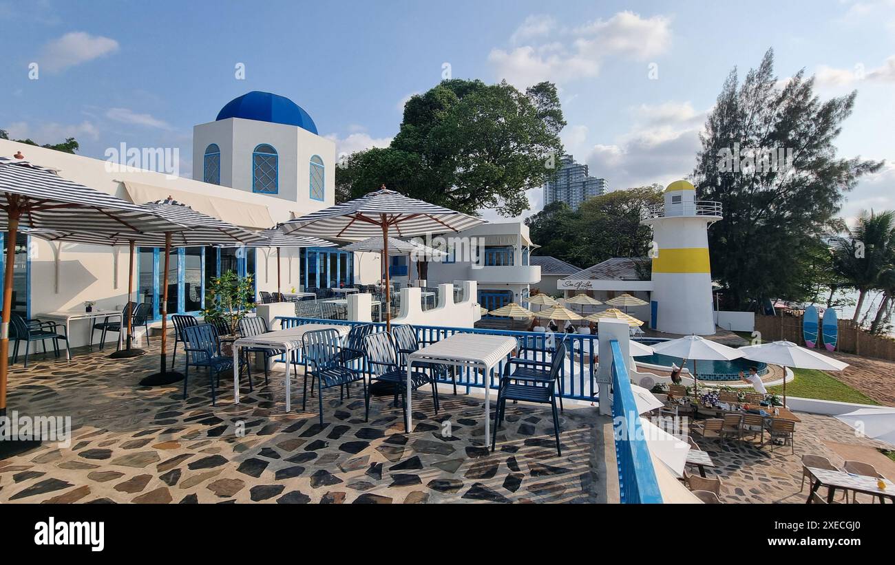 Rilassante zona pranzo all'aperto con tavoli ombreggiati e ombrelloni colorati sullo sfondo di lussureggiante vegetazione e blu chiaro sk Foto Stock