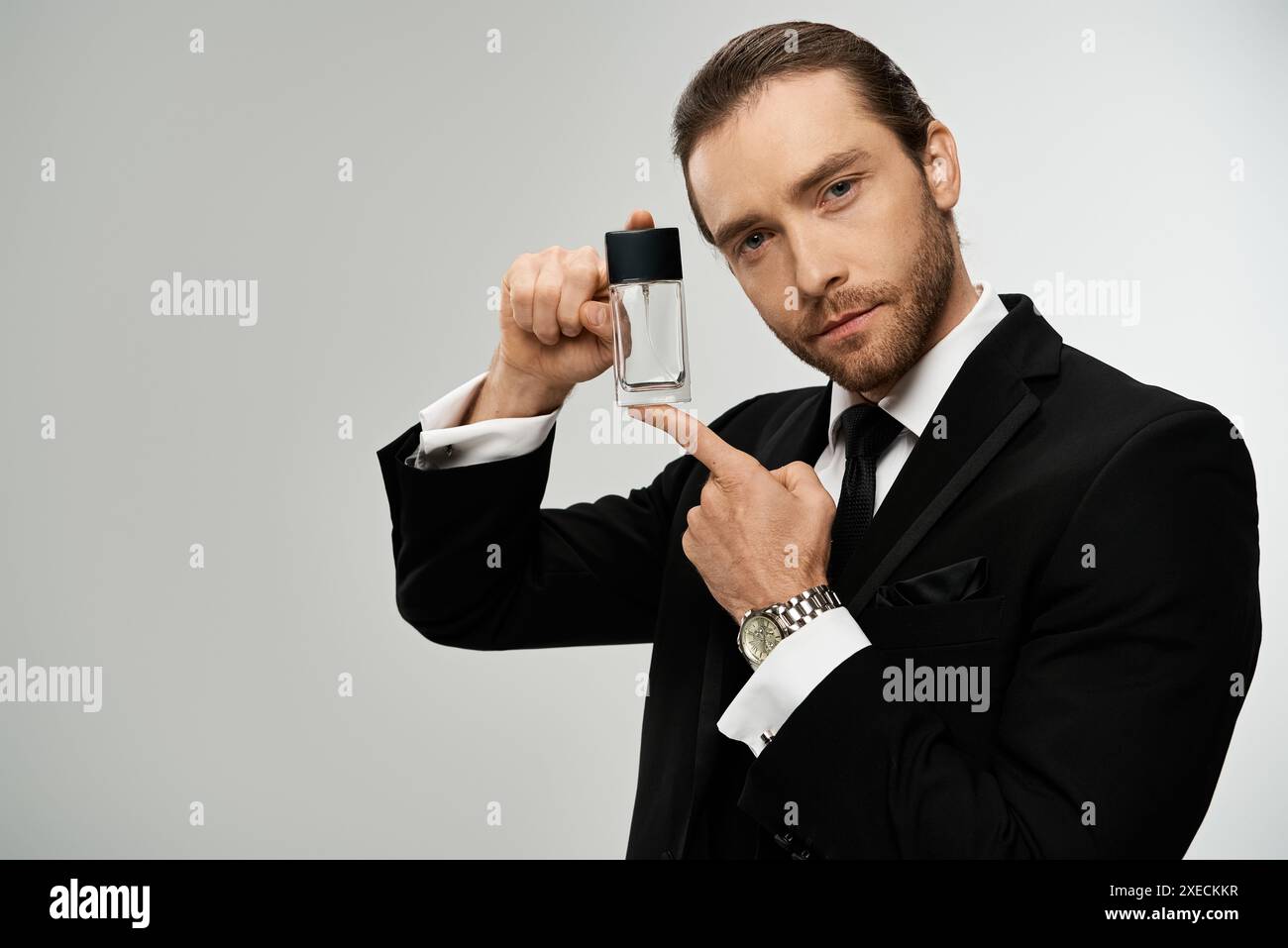 Un bell'uomo d'affari con la barba in costume regge elegantemente una bottiglia di vetro con profumo Foto Stock