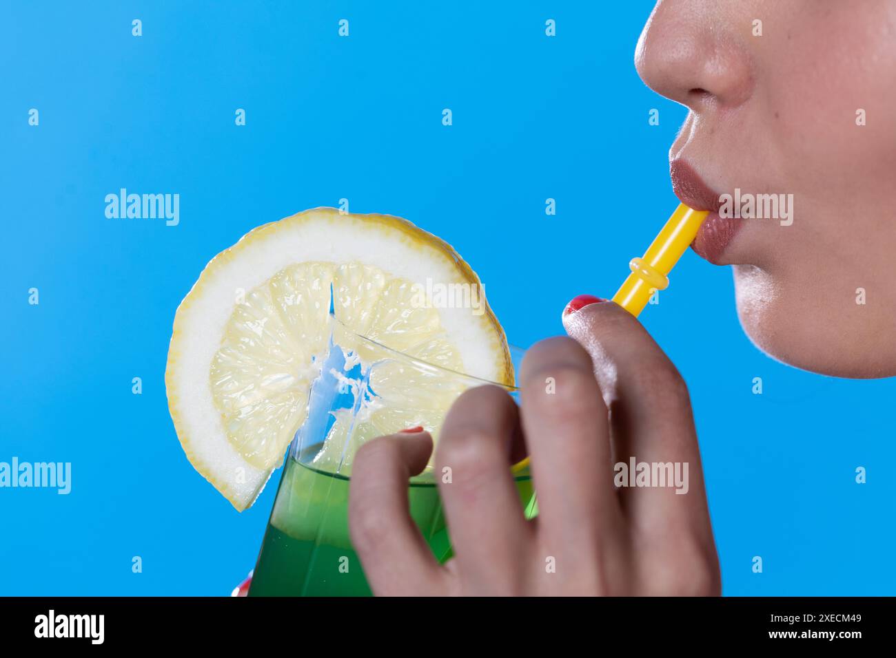 Primo piano di labbra femminili mentre beve una bevanda alcolica fredda verde attraverso una cannuccia. Foto Stock