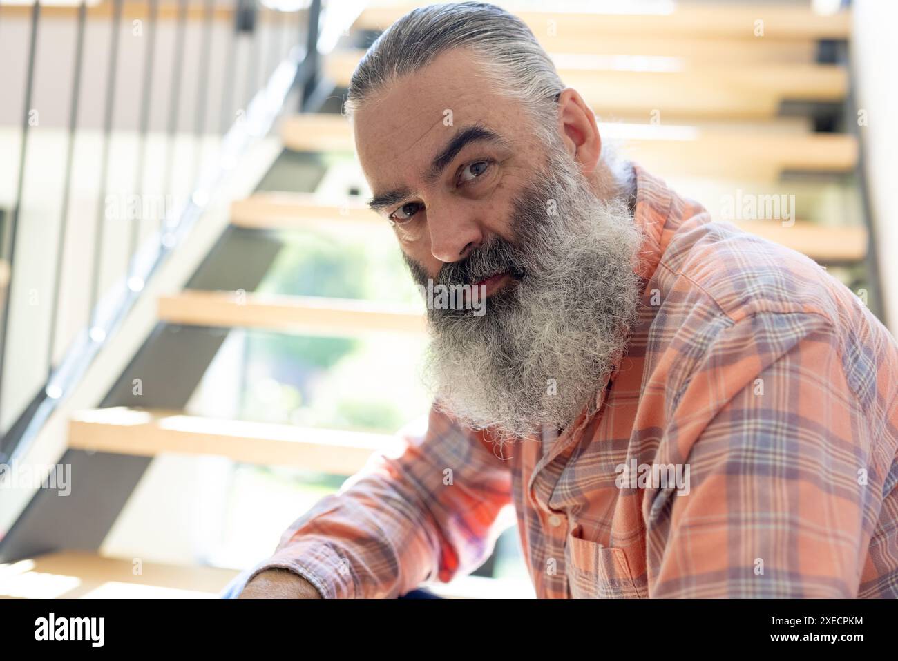 A casa, un uomo anziano con la barba lunga seduto sulle scale, guardando la macchina fotografica Foto Stock
