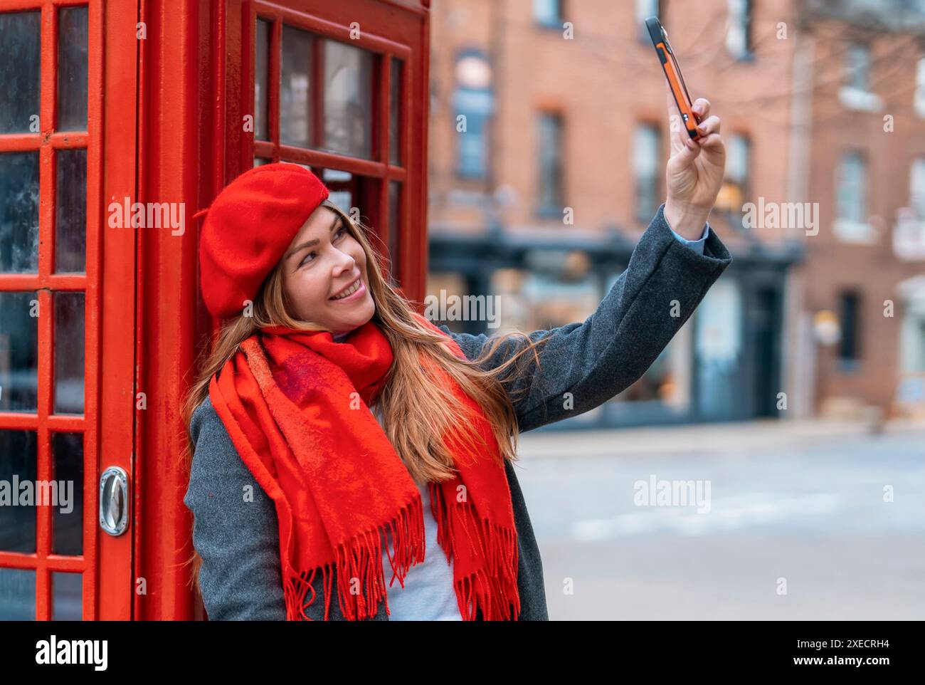 Ritratto esterno di una donna che usa la fotocamera contro il telefono rosso nella città inglese Foto Stock