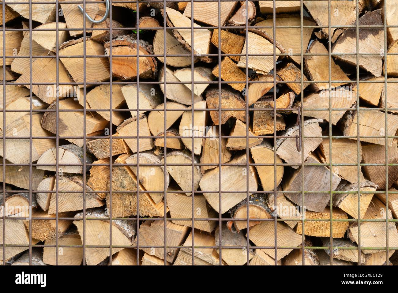 Legno pronto per il forno impilato e segato conservato dietro una griglia metallica. Foto Stock