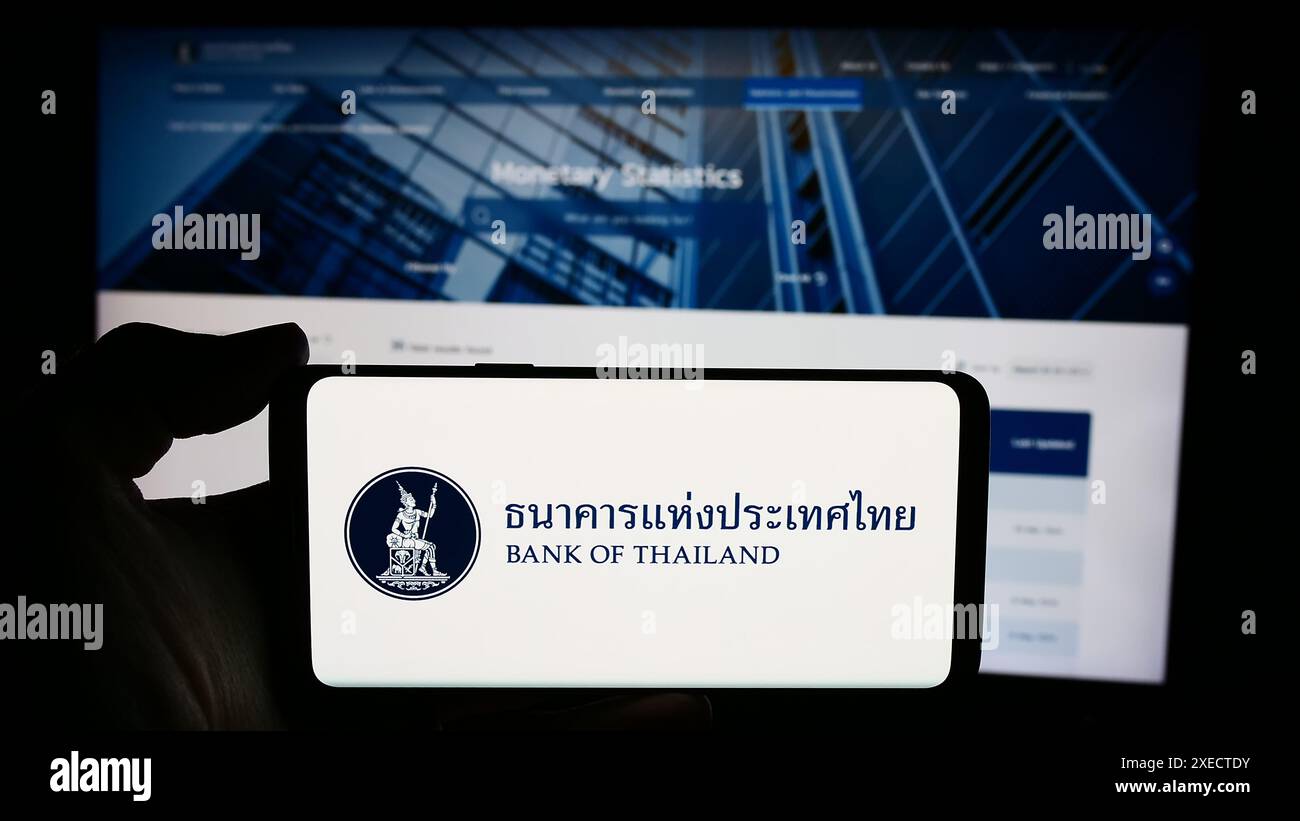 Persona che detiene un cellulare con il logo dell'istituto finanziario tailandese Bank of Thailand (BOT) davanti alla pagina web. Mettere a fuoco il display del telefono. Foto Stock