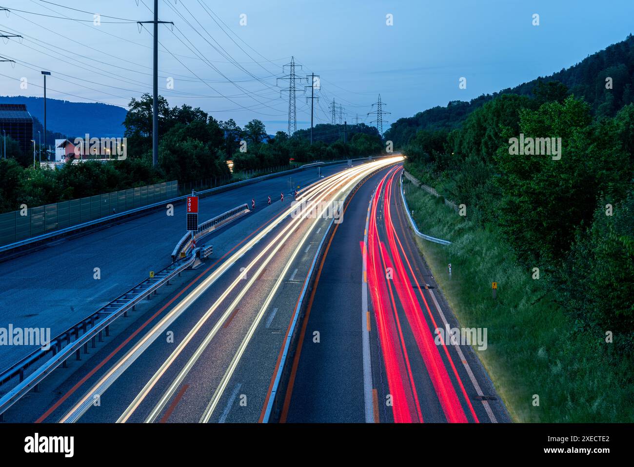 Autostrada con sentieri leggeri di auto di passaggio durante il tramonto. Le piste luminose diventano sempre più luminose con l'ambientazione del crepuscolo. Esposizioni a lungo termine. Scena con Hig Foto Stock