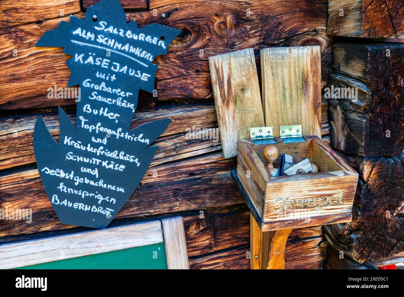 Un cartello alla Filzmoosalm nella valle di Großarl, Salisburgo, Austria, pubblicizza uno spuntino di formaggio „Salzburger Alm Schmankerl" con formaggio acido di Großarl, burro, crema di ricotta, formaggio alle erbe, formaggio semiduro e pane di fattoria fatto in casa. Sotto è appesa una scatola per il timbro della carta dei escursionisti del Salzburger Almenweg. Le fattorie alpine possono offrire solo prodotti della propria produzione. Foto Stock
