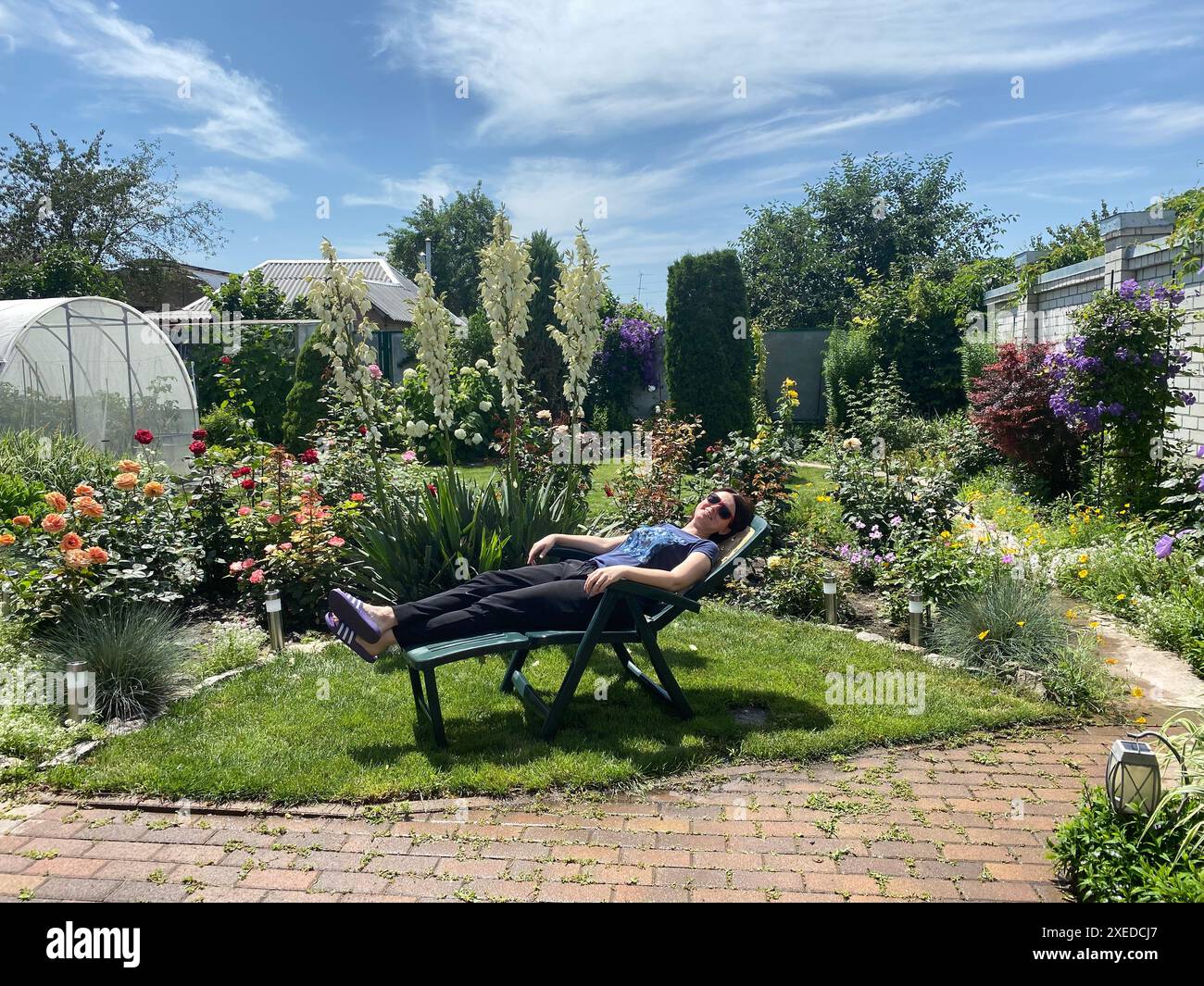 Donna che posa su una sedia reclinabile giardino in cortile di casa Foto Stock