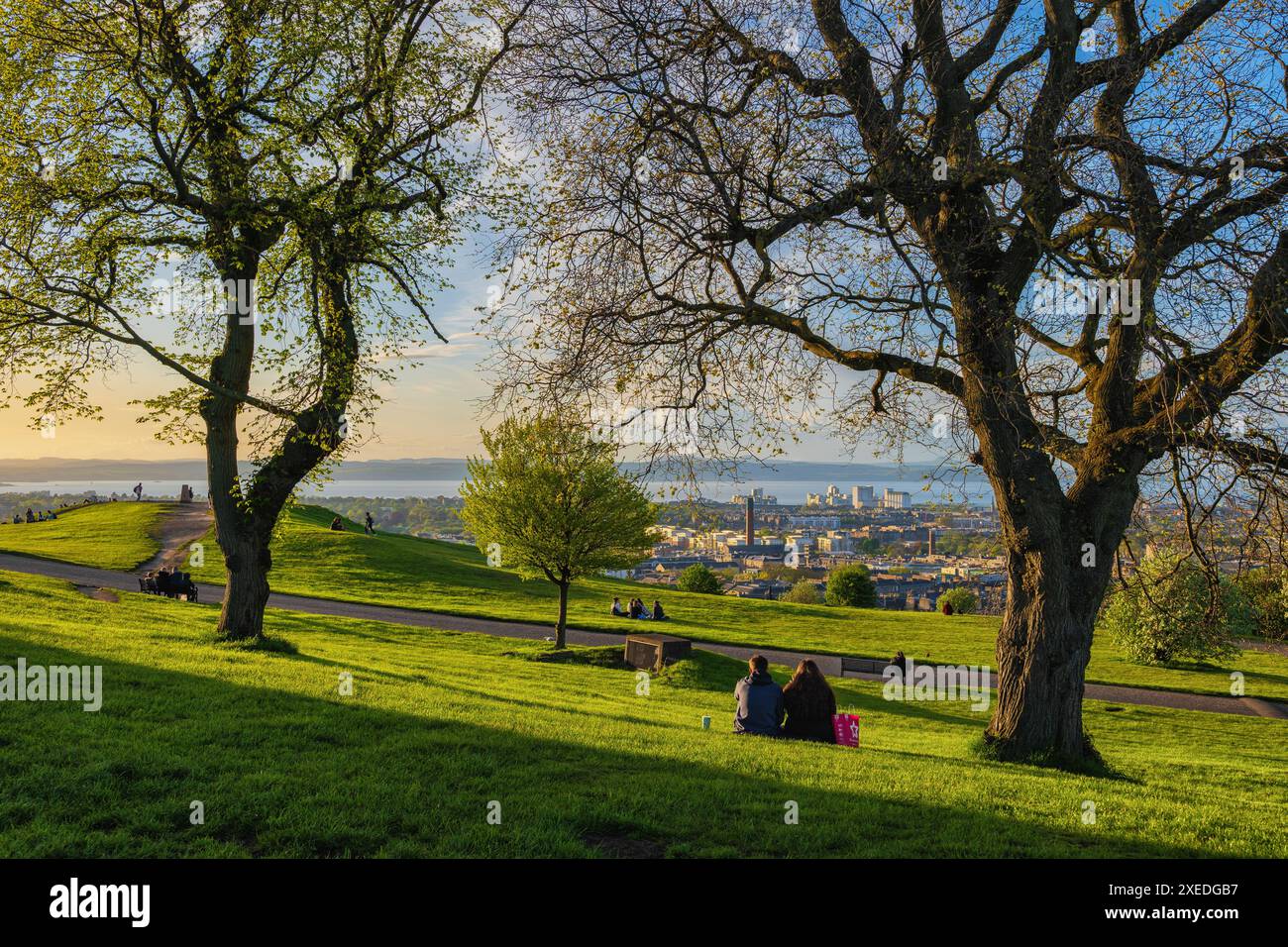 Persone sul parco di Calton Hill al tramonto in primavera con il quartiere di Leith all'estremità finale, la città di Edimburgo in Scozia, Regno Unito. Foto Stock