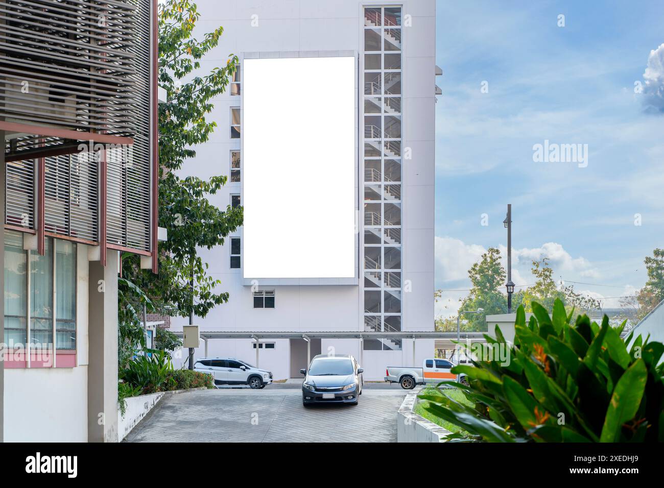 Un grande cartellone bianco sorge sul lato di un alto e moderno edificio. Il cartellone è bianco con uno sfondo bianco, percorso di ritaglio. Le auto sono parcheggiate Foto Stock