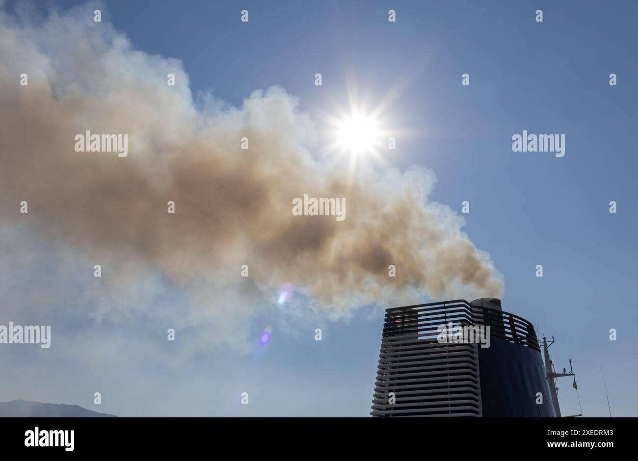 Camino industriale che rilascia fumo sotto un cielo azzurro e limpido con il sole che splende brillantemente, evidenziando l'inquinamento atmosferico e l'impatto ambientale. Foto Stock