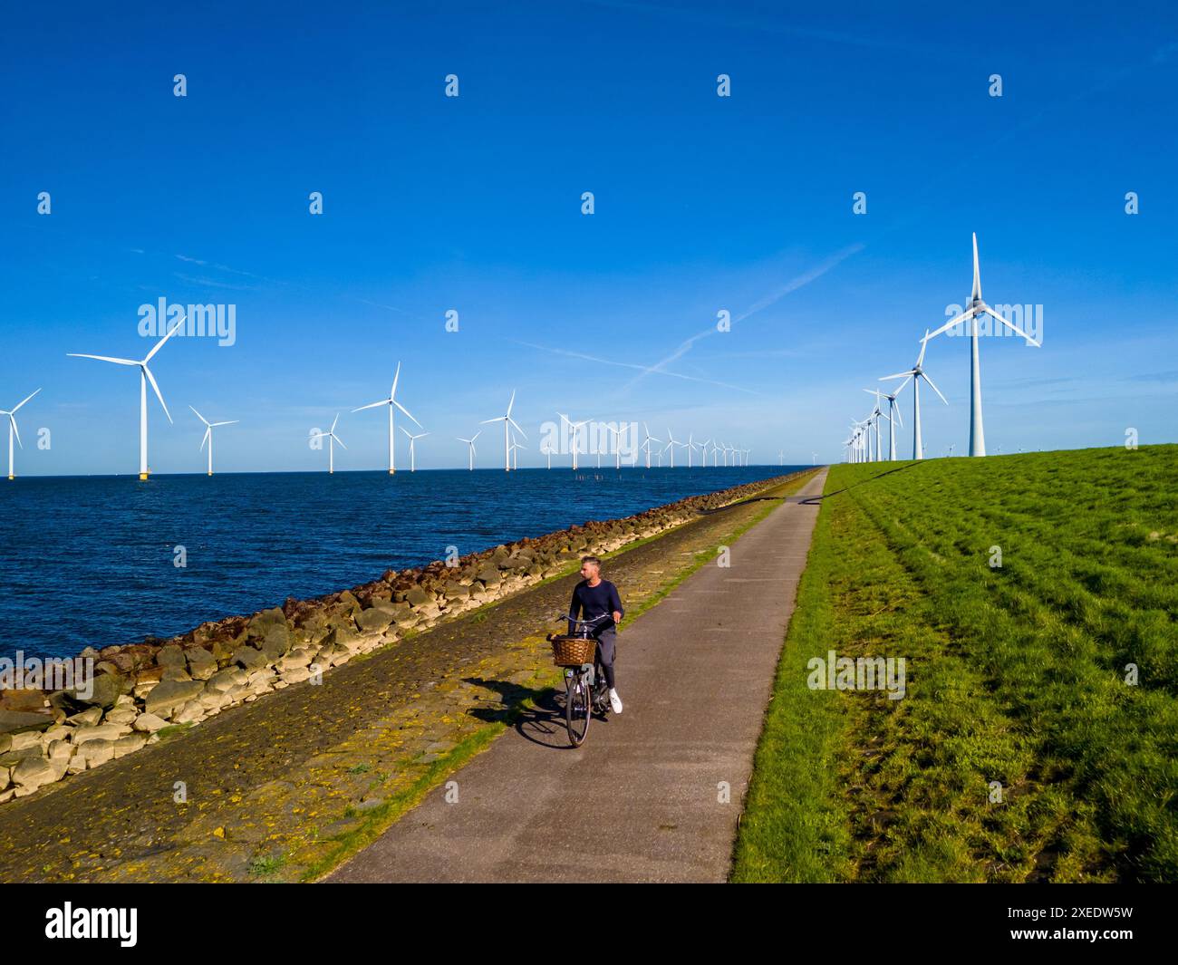 In primavera, un uomo pedala con grazia lungo un pittoresco sentiero vicino alle turbine a vento Foto Stock