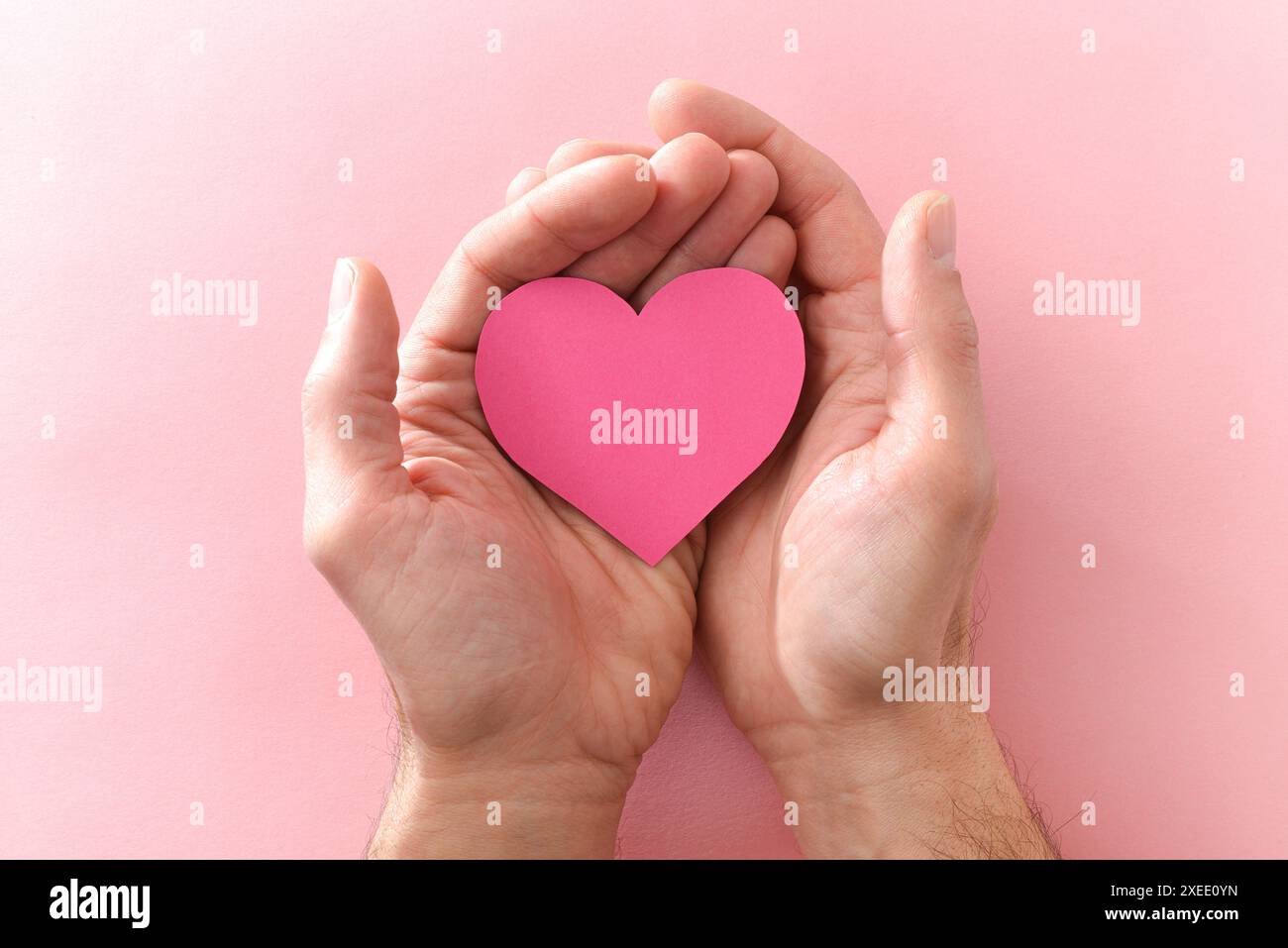 Due mani di un uomo che regge una fessura a forma di cuore su uno sfondo rosa. Vista dall'alto. Foto Stock