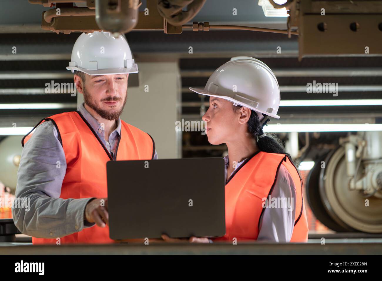 Ingegneri maschi e femmine lavorano insieme in una stazione di riparazione elettrica. Ispezione del sottocarro del treno elettrico b Foto Stock