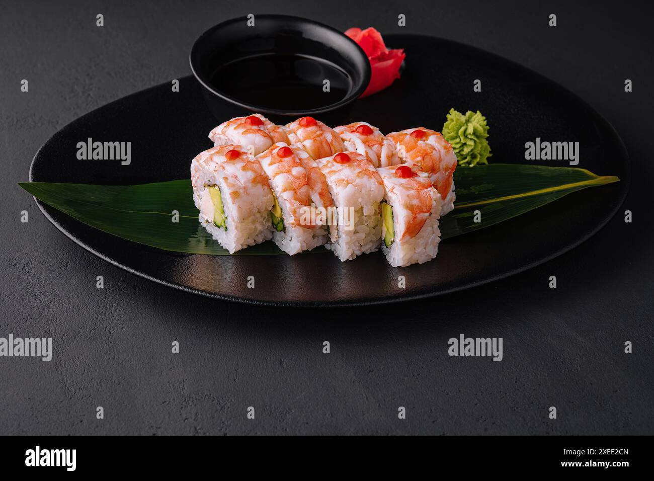 Rotolo di sushi ricoperto di carne di gamberi su piastra di ceramica nera Foto Stock