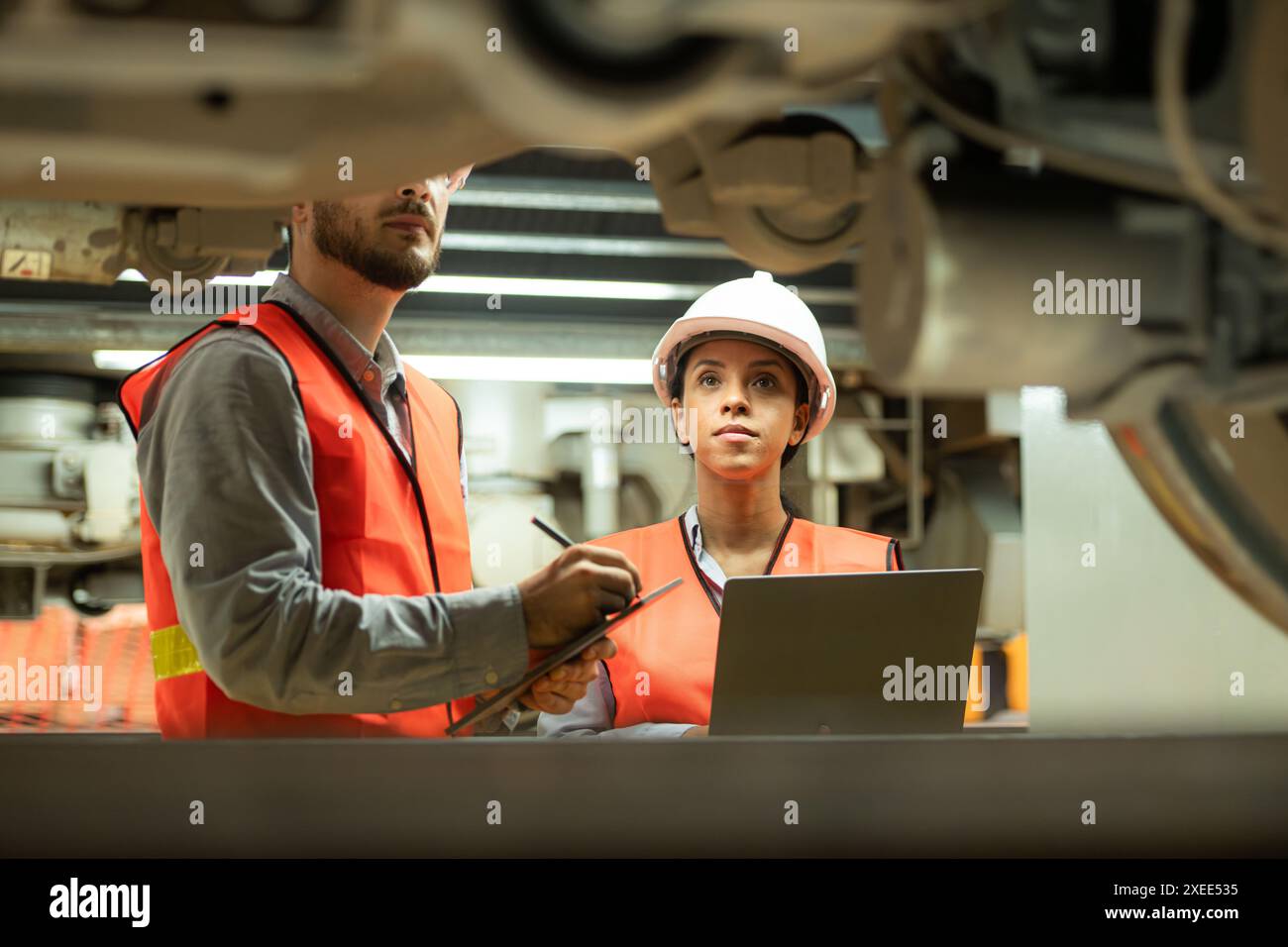 Ingegneri maschi e femmine lavorano insieme in una stazione di riparazione elettrica. Ispezione del sottocarro del treno elettrico b Foto Stock
