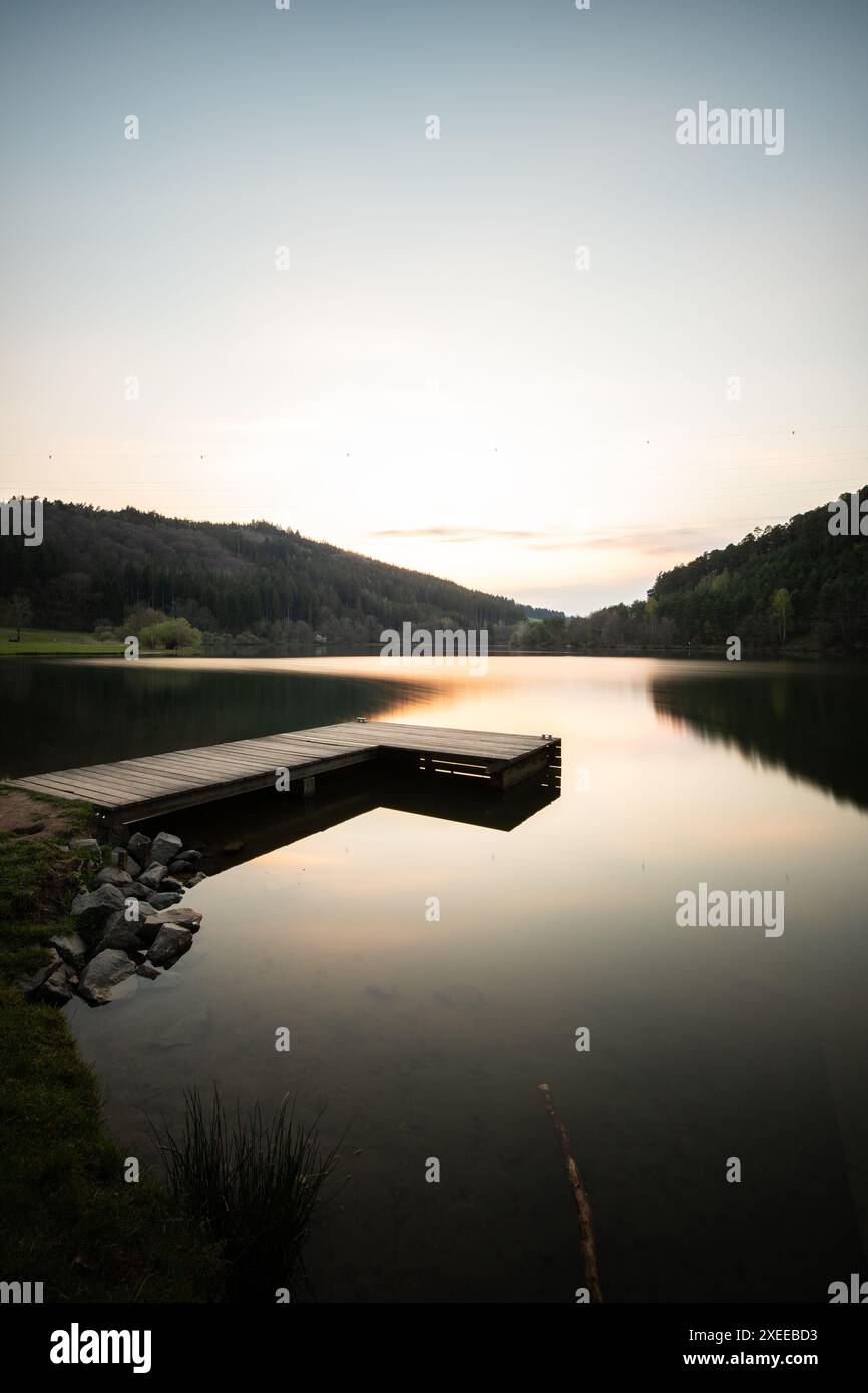 Tramonto su un lago tranquillo in una valle circondata da una foresta. Bacino idrico di Marbach Foto Stock