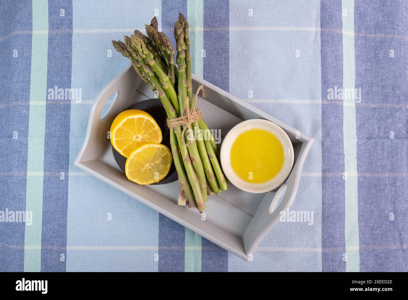 Impasto di asparagi freschi su un vassoio di legno con limone e olio d'oliva su una tovaglia a quadri blu Foto Stock