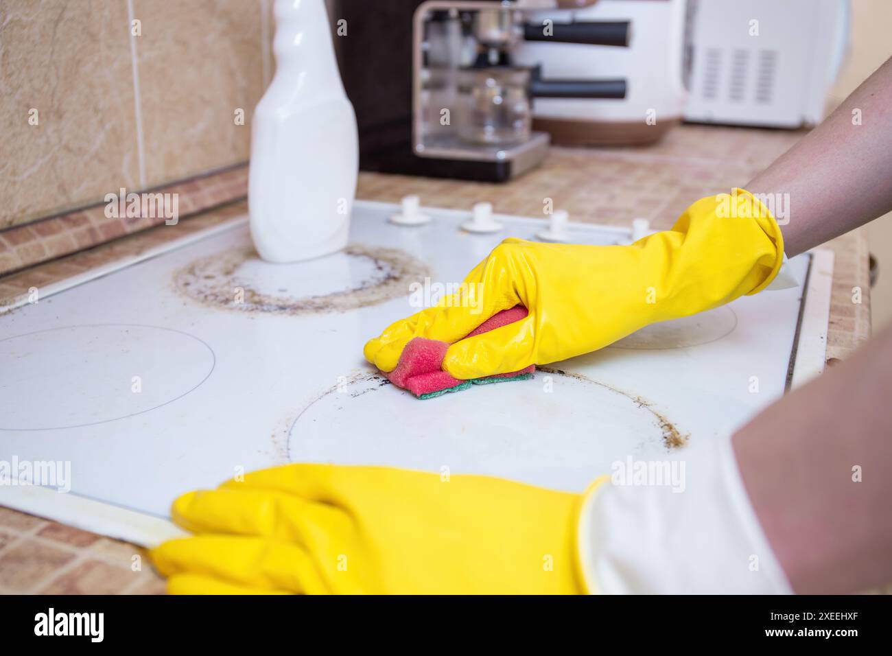 Mani con guanti gialli che puliscono una stufa sporca da cucina con una spugna, pulizia e lavori domestici Foto Stock