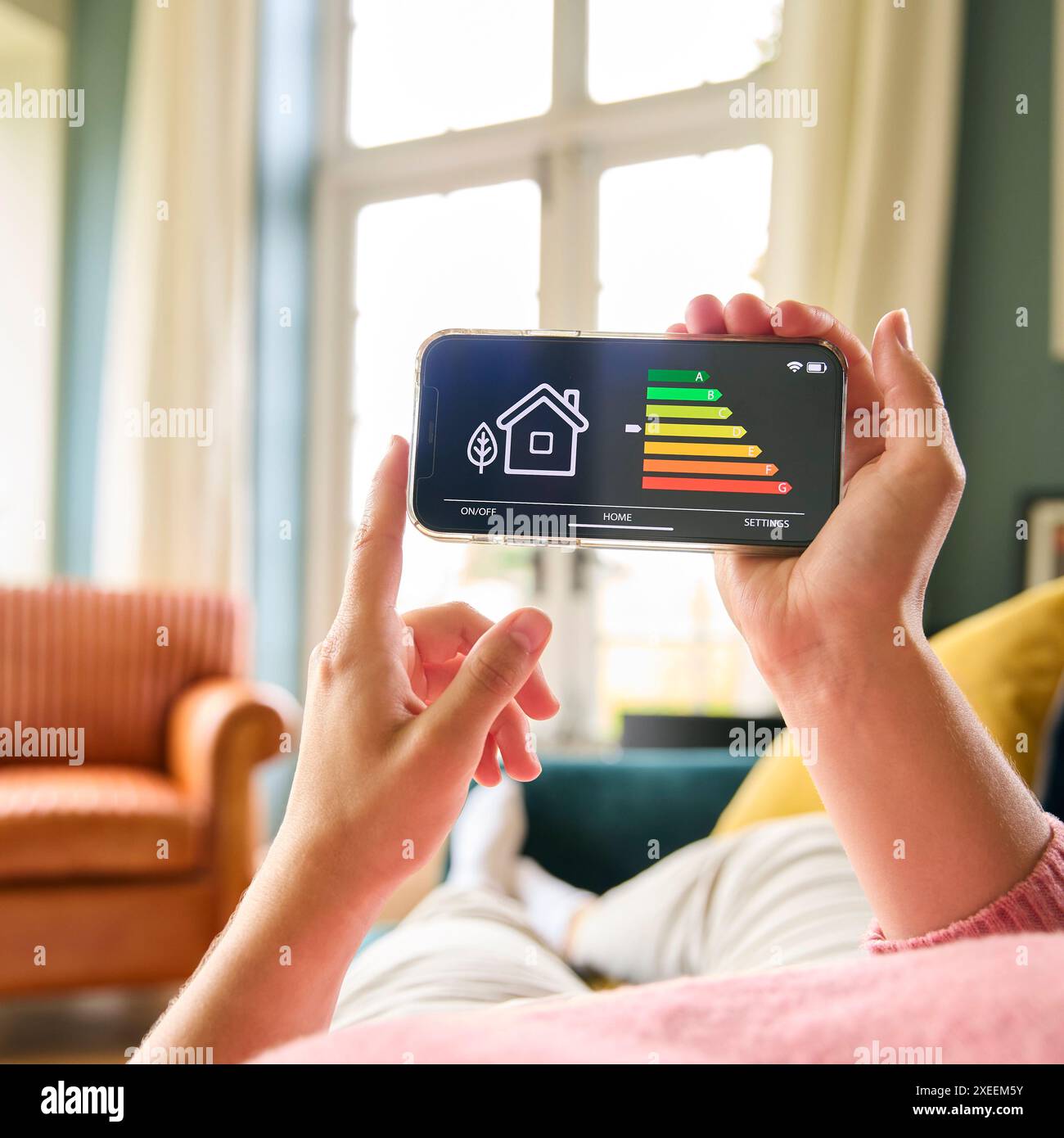 Primo piano di una donna che guarda lo schermo del misuratore di efficienza energetica su un telefono cellulare disteso sul divano di casa Foto Stock