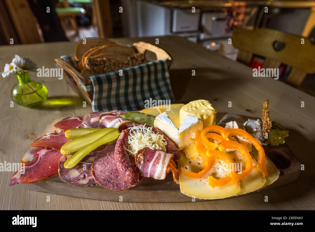 Un vassoio di snack, una Jausenplatte, con formaggio acido, Camembert, burro, formaggio a pasta dura, pancetta, prosciutto e salsiccia è posato su un tavolo di legno alla Filzmoosalm nella valle di Großarl, Salisburgo, Austria. Accanto ci sono un cestino di pane fatto in casa e un vaso di margherite. Tutti gli ingredienti provengono dalla produzione propria dell'alm. Foto Stock