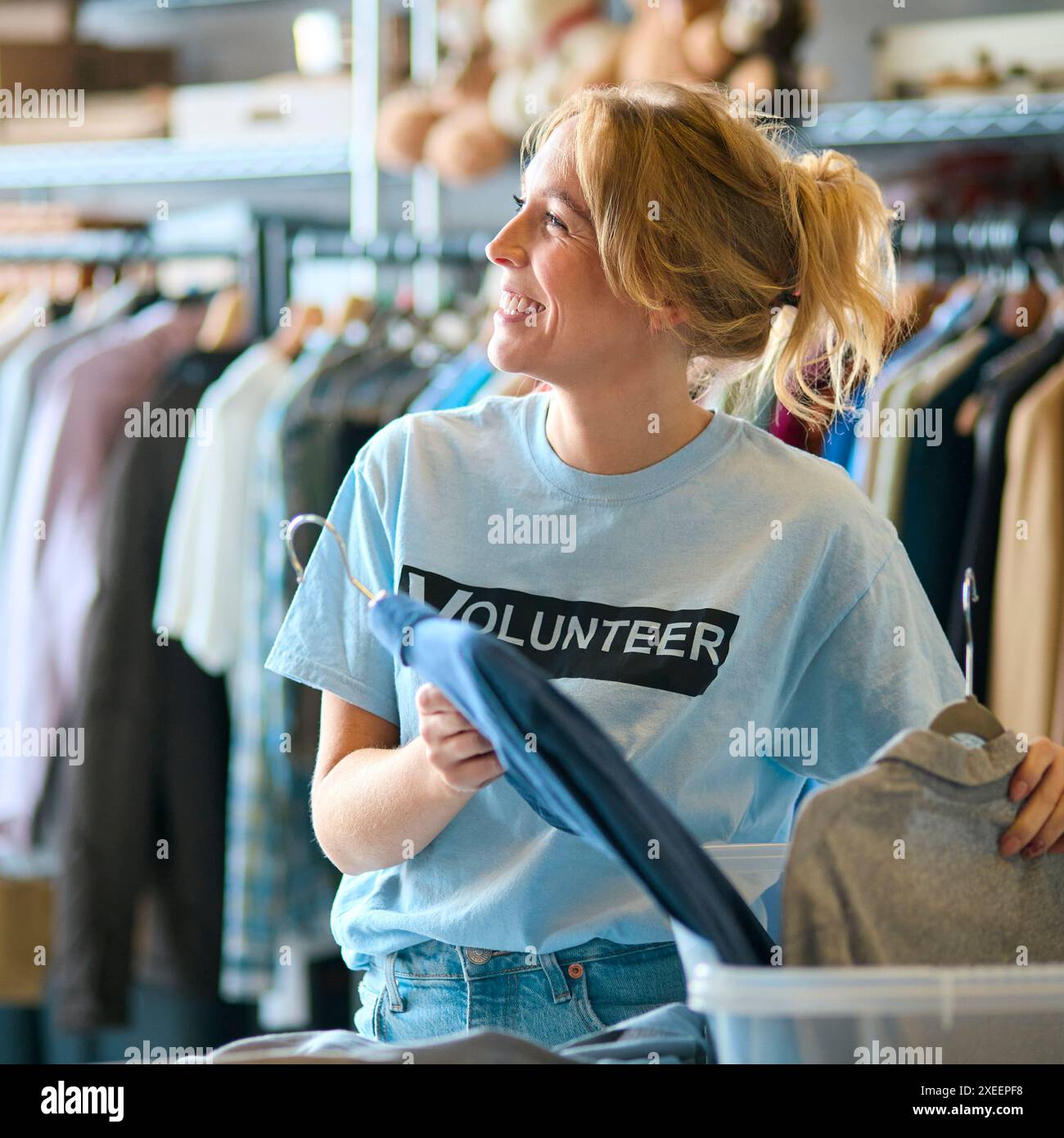 Lavoratrice di beneficenza femminile che seleziona le donazioni di abbigliamento al Thrift Store Foto Stock