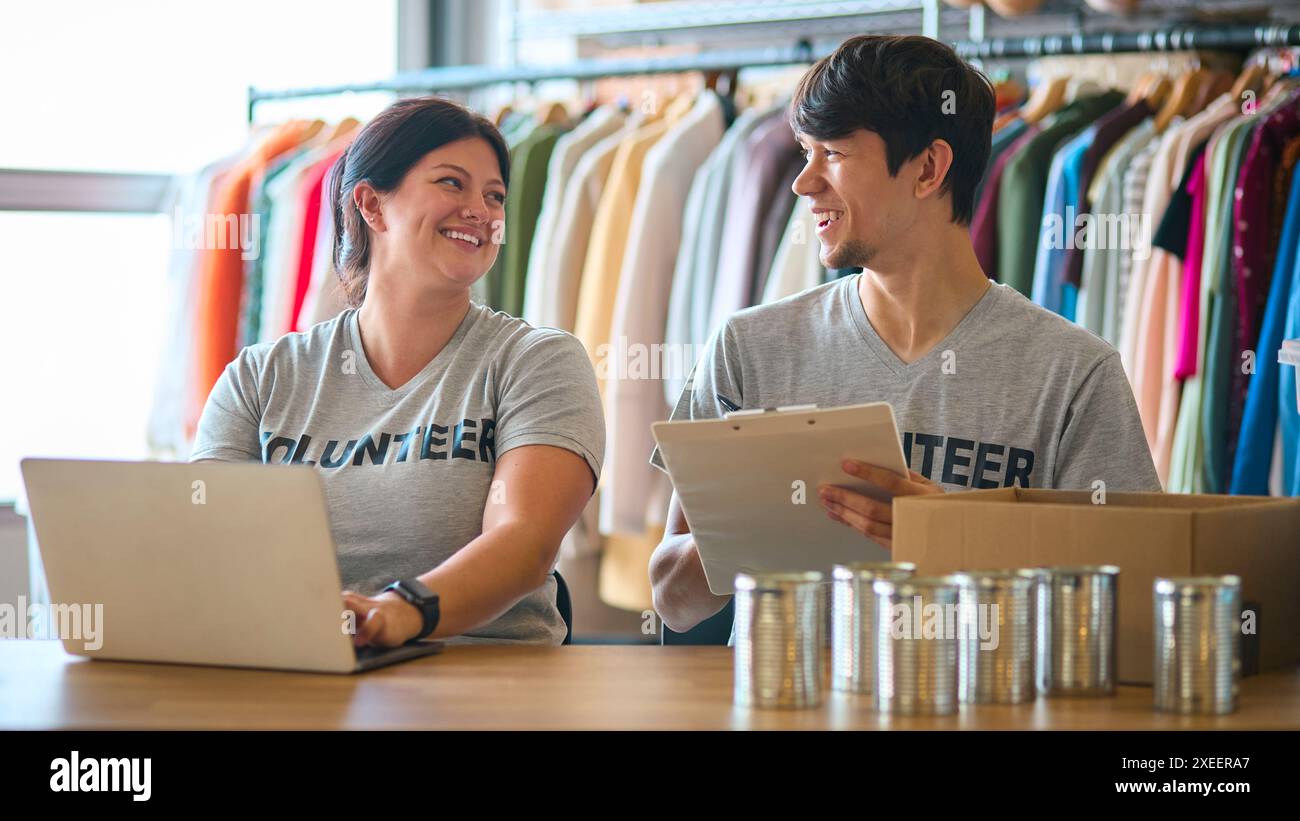 Lavoratori di beneficenza uomini e donne alla scrivania con laptop che controllano le donazioni di abbigliamento al Thrift Store Foto Stock