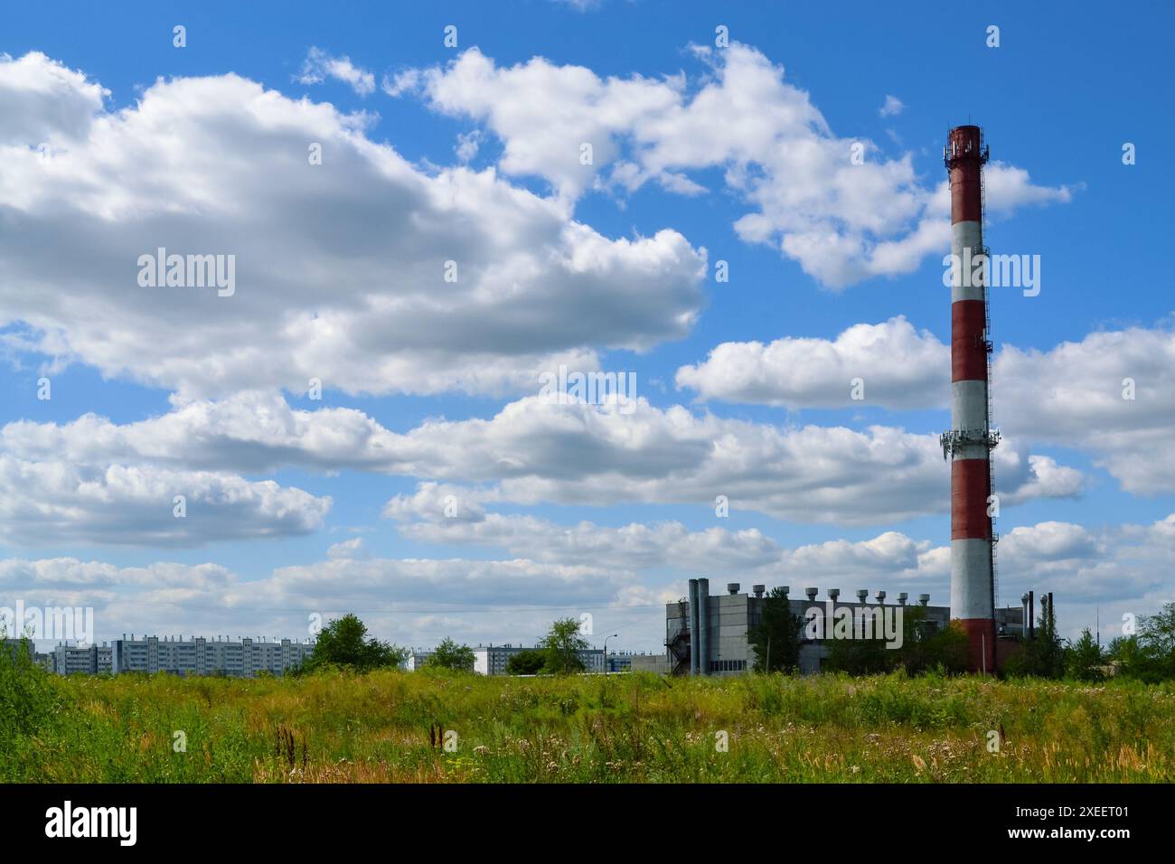 Alto camino rosso e bianco a righe di una caldaia sullo sfondo di nuvole bianche nel cielo blu Foto Stock